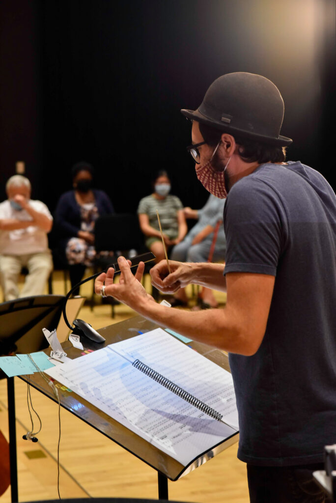 A man wearing a bowler hat conducts musicians from sheet music on a stand
