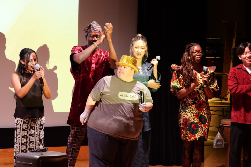 A group of performers raise their joined hands together on stage in celebration