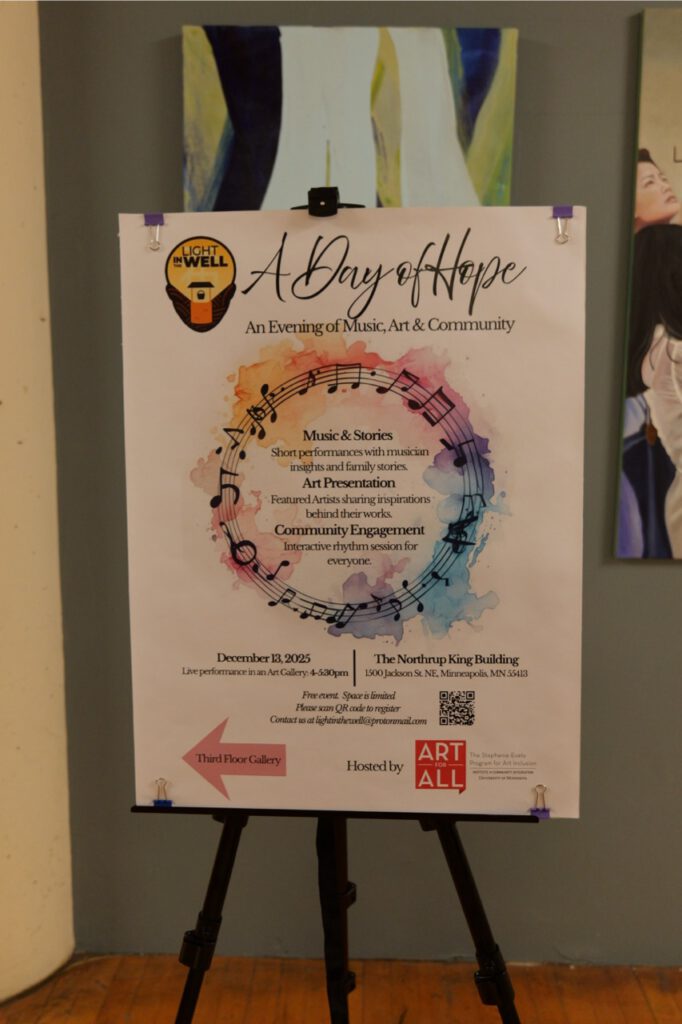 Event poster for "A Day of Hope: An Evening of Music, Art & Community" displayed on a black easel inside an art gallery space.