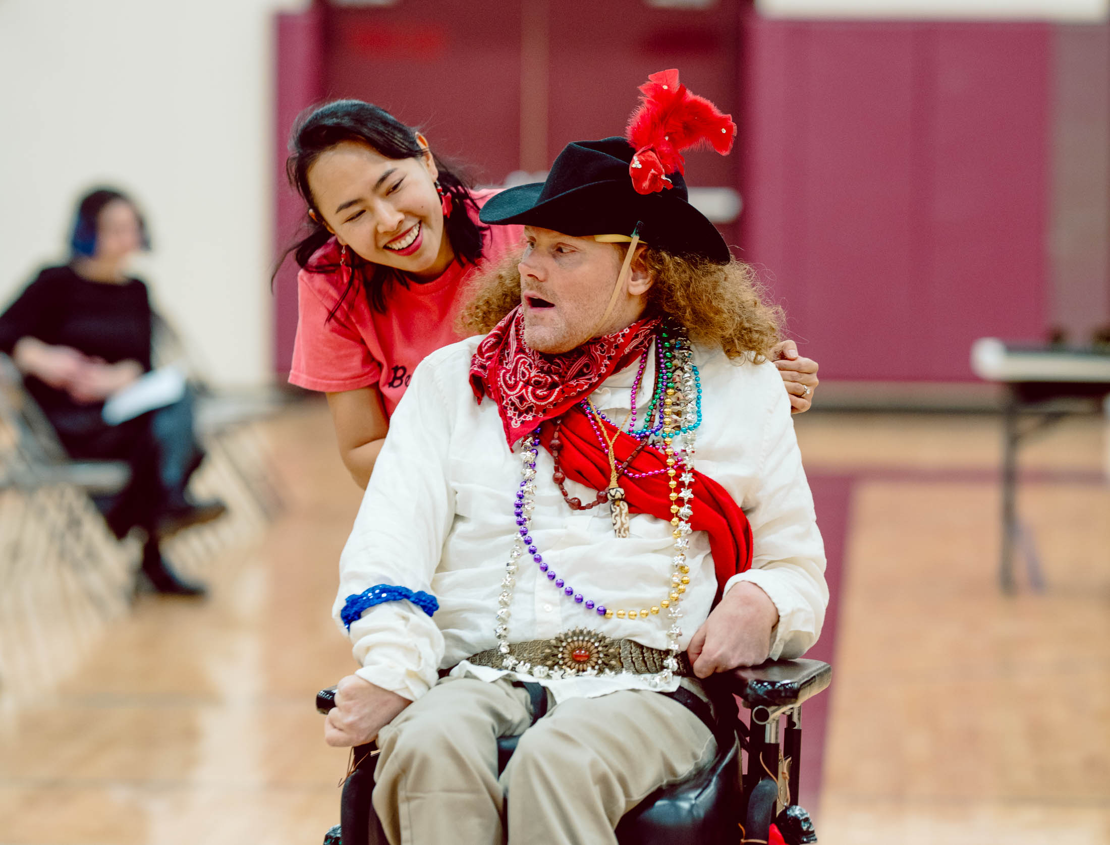 Smiling woman leaning toward a man in a wheelchair dressed in a pirate costume with beads and a feathered hat