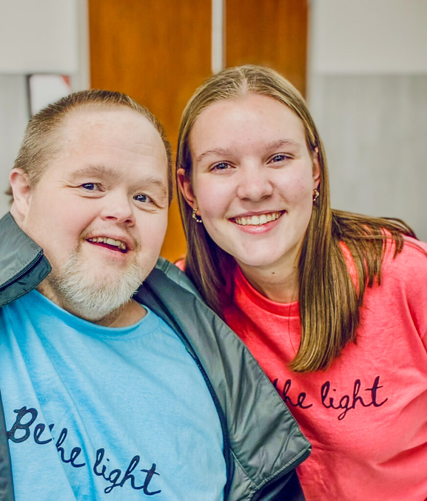 A man and a teenage girl in matching "Be the light" T-shirts smiling together