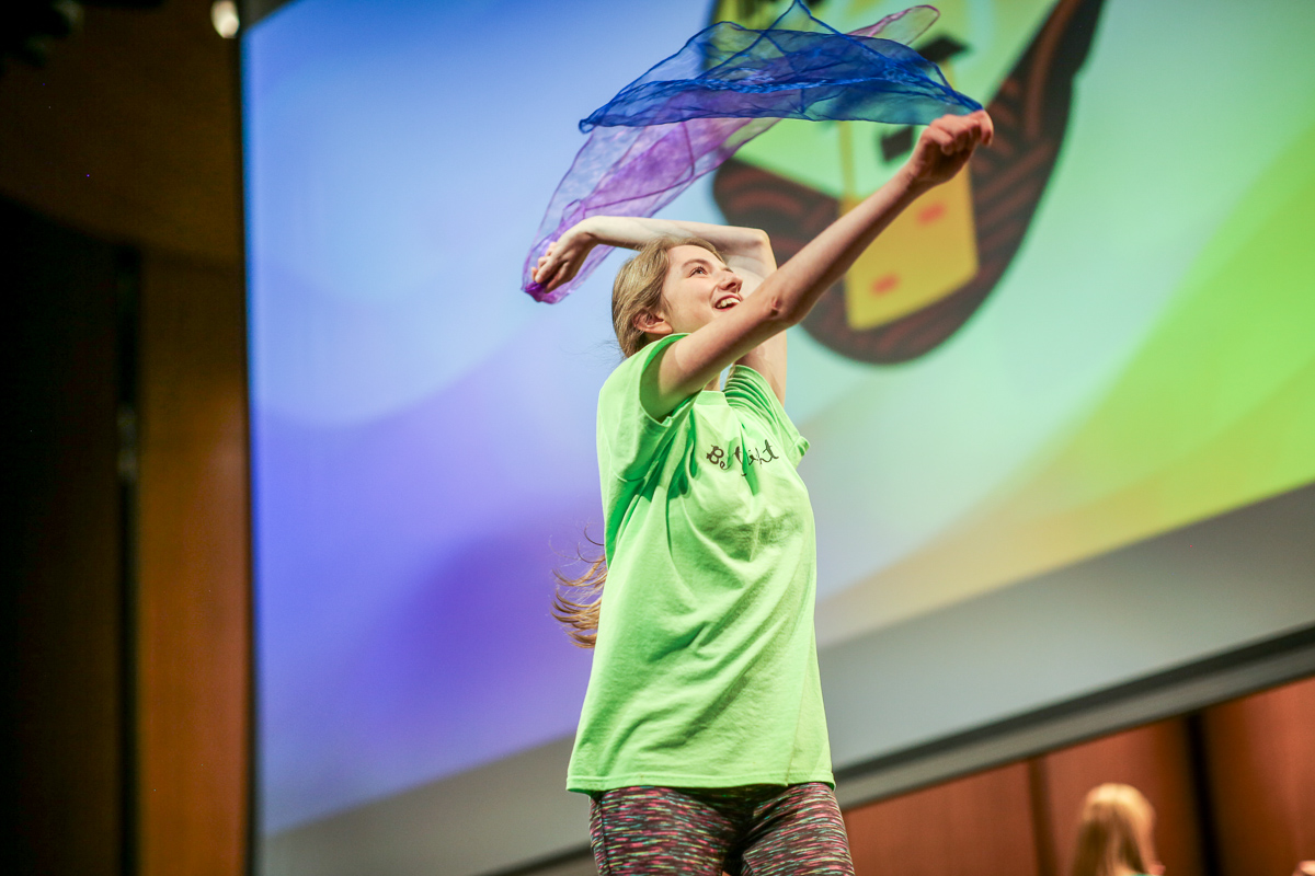 A dancer on stage swings blue and purple scarves overhead