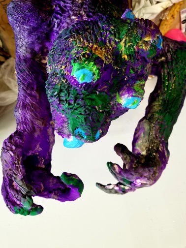 Close-up of the same dragon sculpture, showing its textured head and clawed hands painted in purple, green and turquoise